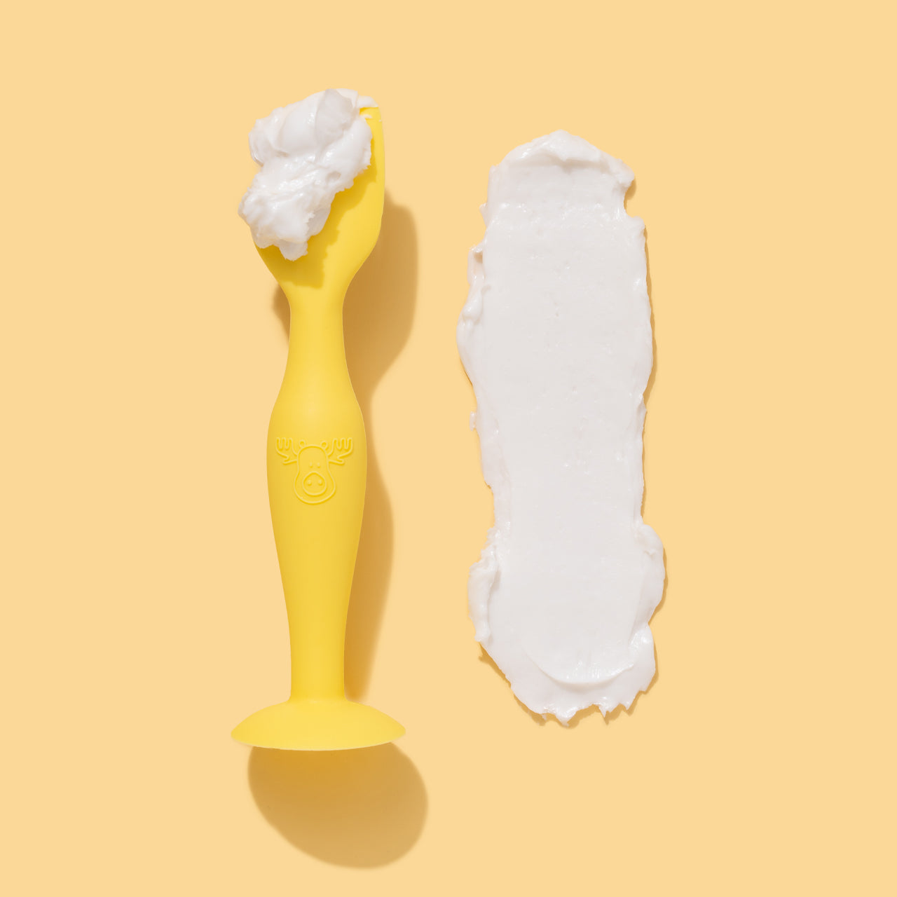 Tubby Todd Spatula laid on it's side with a scoop of cream on it and a smear of cream next to it on a yellow background.